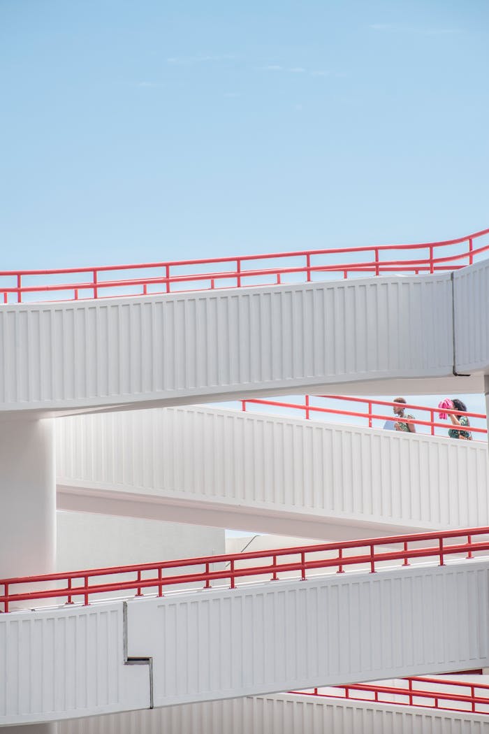 Elegant footbridge with red railings under a clear blue sky in a modern cityscape.